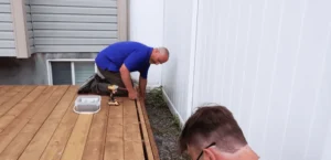 Two contractors installing a wooden deck, focusing on precision and alignment. Build your perfect outdoor space with expert craftsmanship today!