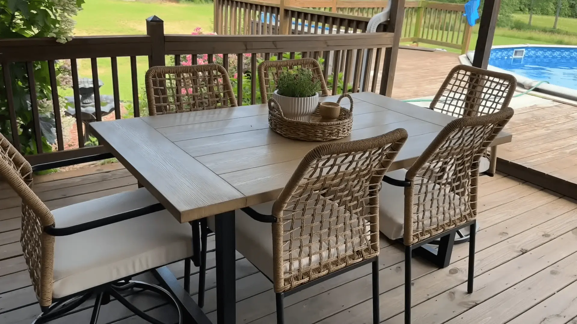 Cozy outdoor dining area on a wooden deck with wicker chairs, a table, and a view of a pool. Click here to discover creative ideas for decorating your pool deck.