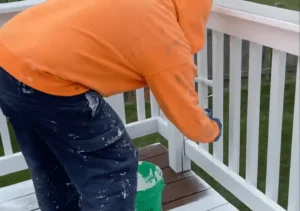 Contractor carefully painting a white deck railing. Hire a professional to ensure your deck's paint job is done right.